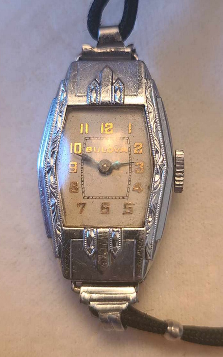  Off-white dial, gold arabic numbers and gold "Bulova" on dial, blue minute and hour hands. The case has a tonneau shape featuring art deco ornamentation.