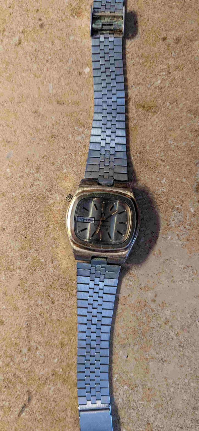 Gold, square-faced watch with Bulova Accutron text, tuning fork symbol, and date/day window